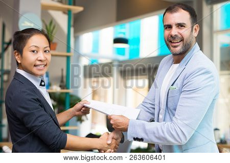 Happy Latin And Asian Partners Shaking Hands And Passing Paper. Multiethnic Managers In Smart Suits 