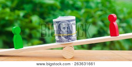 Wooden Figures Of People On Scales And Dollars Between Them. A Dispute Between Two Businessmen. Tria