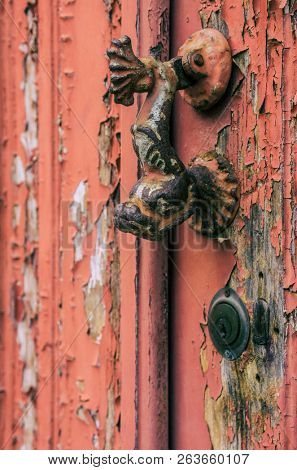 Fish shaped door knocker on an old wooden door with red peeling paint