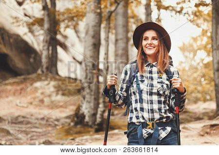Happy Beautiful Young Woman Wearing Brown Hat Walking With Trecking Poles And Looking On The Forest 
