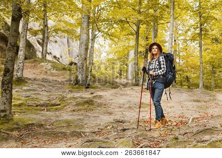 Serious Young Woman With Backpack Wearing Brown Hat, Plaid Shirt, Jeans And Brown Boots Walking With
