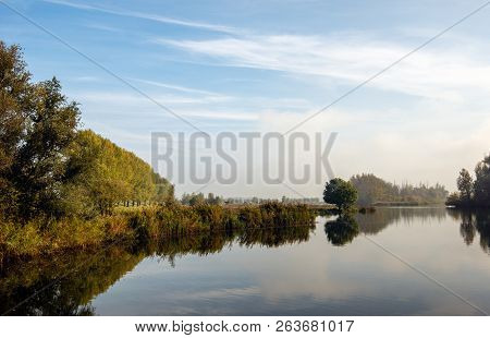 Trees And Bushes Around A Dutch Lake With A Mirror-smooth Water Surface. The Photo Was Taken In Autu