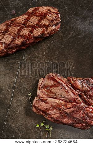 Hot Grilled Whole Denver Steak and Gaucho Steak on Black Stone Background. Fresh Juicy Medium Rare Beef Grillsteak. Barbecue Meat Top View Close Up