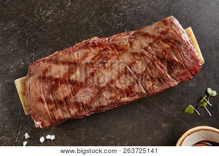Hot Grilled Whole Flank Steak on Black Stone Background. Fresh Juicy Medium Rare Beef Grillsteak. Barbecue Meat Top View Close Up