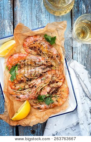 Traditional fried black tiger prawn with lemon and white wine as top view in a white casserole on a wooden blue board 