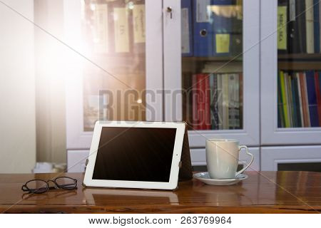 Mock Up Image Of White Tablet Pc With Black Blank Screen And Coffee Cup On Wooden Table In Blur Offi