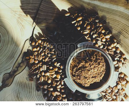 Close Up Of A Metal Portafilter Filled With Coffee Powder And Coffee Beans Around On Wooden Table