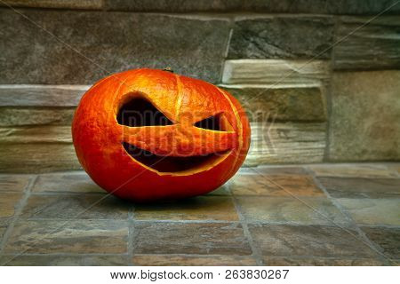 Halloween Pumpkin Stands On A Green Carpet Against A Stone Wall. Jack O` Lantern