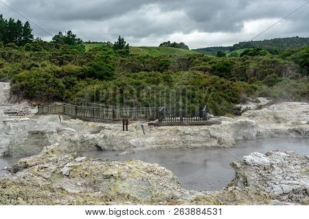 Photo Of A Hot Geothermal Pool Bordered By Trees With Green Hills In The Background.