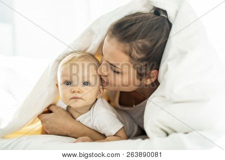 Portrait Of Young Mother With Infant Baby Girl Liying On The Bed Covered With A White Blanket
