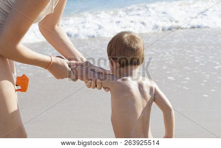 Mother Applying Sunblock Cream To Her Little Son On Back. Idyllic Beach Background