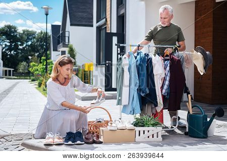 Appealing Blonde-haired Woman Wearing Striped Dress Looking At Shoes At Yard Sale