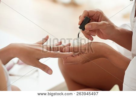 Hands Of Woman Applying Base Coat On Nails Of Her Friend