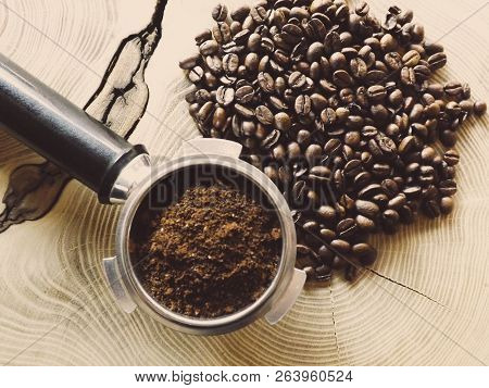 Close Up Of A Metal Portafilter Filled With Coffee Powder And Coffee Beans Around On Wooden Table