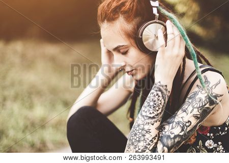 Young Girl With Tattoo And Dreadlocks Listening To Music In The Park