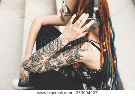 Young Girl With Tattoo And Dreadlocks Listening To Music While Sitting On The Steps