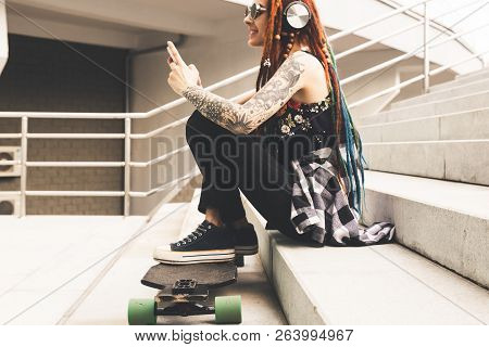Young Girl With Tattoo And Dreadlocks Listening To Music While Sitting On The Steps