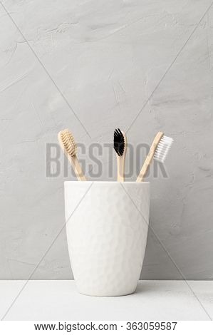 Three Bamboo Toothbrushes In A White Glass. Zero Waste And Without Plastic. Copy Space, Vertical Ori