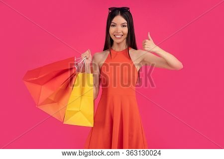 Beautiful Happy Asian Woman Posing Isolated Over Pink Wall Background Holding Shopping Bags Pointing