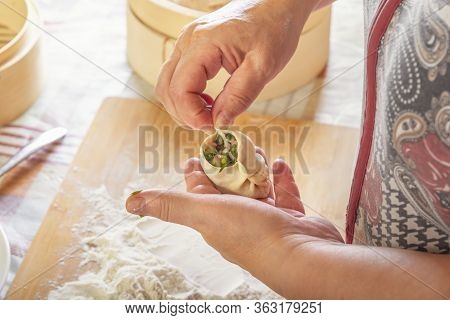 Female Hands Make Manti, Khinkali, Dumplings Or Wonton From Dough With Minced Meat Filling And Green