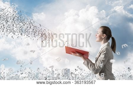 Smiling Woman Looking At Flying Out Random Letters From Opened Book. Elegant Young Woman In White Bu
