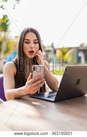 Shocked Woman Look At Phone, Uses Laptop Computer For Online Communication Beach Terrace Cafe