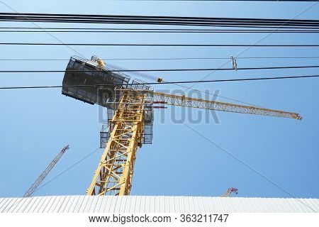 Construction Crane And Power Lines With Blue Sky Background. Low Angle Shot.