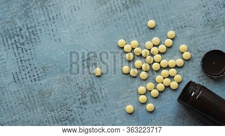 Yellow Round Tablets Or Pills Vitamins Flat Lay On Blue Stone Concrete Table With Black Plastic Bott