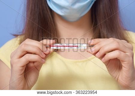 Horizontal Shot Of Unknown Female With Short Hair Holding Thermometer In Both Hands, Wearing Antibac