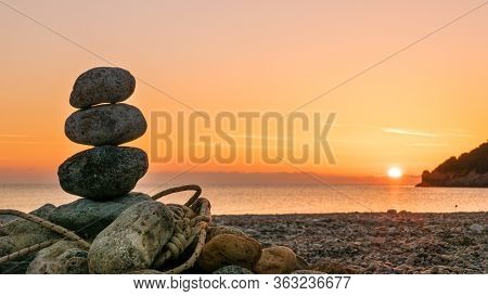 Beach Stone Fireplace With Rope At Sunrise. Sea Water With Rocks In The Background. Vlychada Beach P