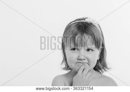 A Little Girl Grimaces Against A White Background. The Child Is Up To Something. Concept Of Emotions
