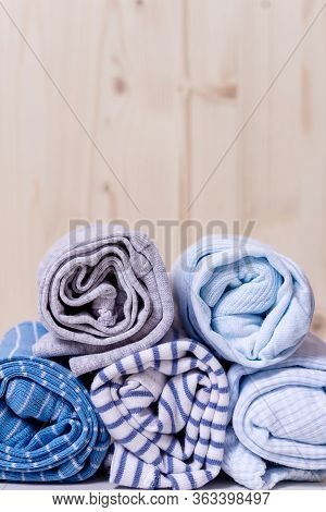 Clothes Stack For Newborn Boy. Close Up Of Rolled Up Kids Chlothes In Front Of Wooden Wall. Grey And