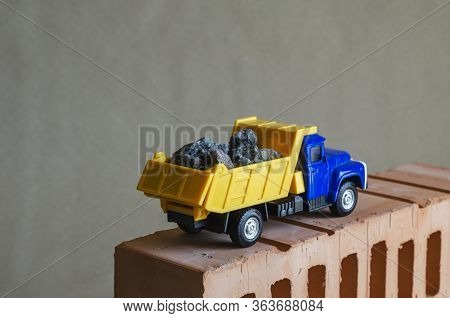 Yellow Dump Truck Rides On Top Of A Brick. Toy Truck With A Full Body Of Building Materials. Creativ