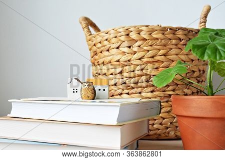 Wicker Basket, Books, Green House Plant In Terracotta Pot, Ceramic Houses And Owl Over White