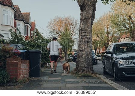 London, Uk - April 22, 2020: Rear View Of A Man Walking His Dog On A Pavement In From Of The Houses 