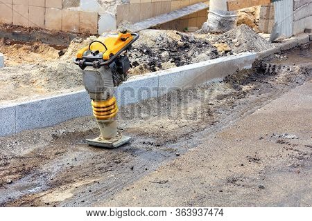 Petrol Vibro Rammer Is Used On A Hard-to-reach Working Place In The Background Of A Road Constructio