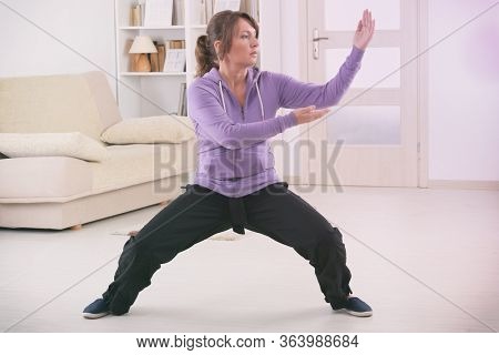 Beautiful woman doing qi gong tai chi exercise at home