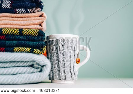 Stack Of Folded Woolen Checked Blankets And Mug In Wollen Cover, Autumn And Cold Winter Concept