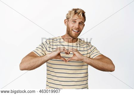 Smiling Blong Man Showing Hand Heart Gesture, I Love You Sign, Likes Something, Standing Over White 