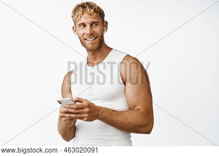 Portrait Of Smiling Strong Sportsman With Mascules, Holding Smartphone, Using Sport App, Standing Ov