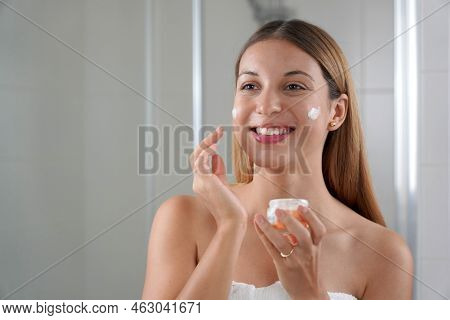 Young Woman Applying Cream On Her Cheeks. Wellness Treatments For Teenage Sensitive Skin Concept.