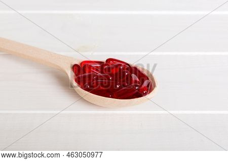 Vitamin Capsules In A Spoon On A Colored Background. Pills Served As A Healthy Meal. Red Soft Gel Vi