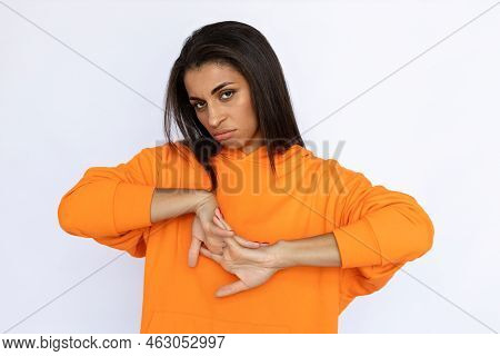 Young Hispanic Woman Cracking Fingers. Female Model In Orange Hoodie Looking At Camera With Bored Fa
