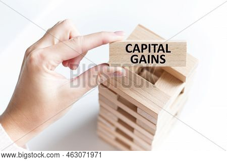 Capital Gains Text On A Wooden Bar In A Man's Hand On A Light Background, A Business Concept