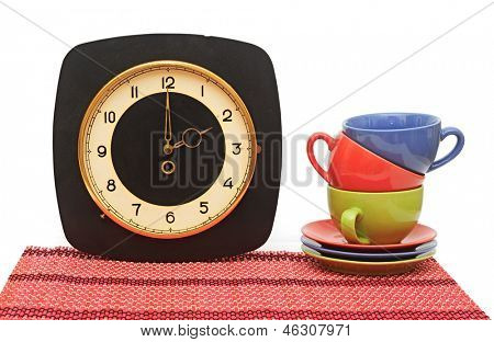 Set van kleurrijke kopjes met oude muurklok op wit. Tea time