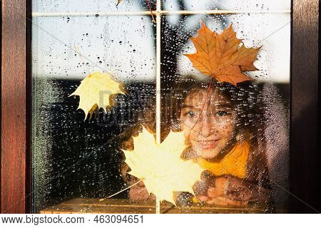 Child Looks Out Of The Window Of The House Outside, Autumn Weather, Wet Glass With Drops After Rain,