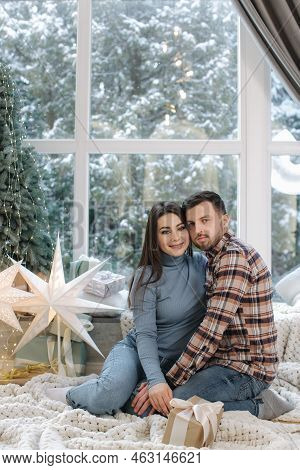 Young And Beautiful Couple Of Man And Woman Sitting In Front Of Big Windor, Its Snow Outside. Happy 