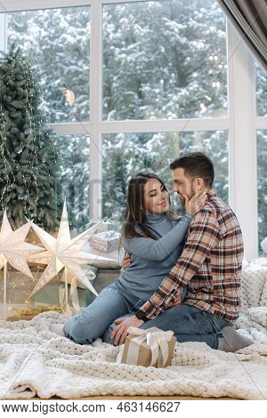 Young And Beautiful Couple Of Man And Woman Sitting In Front Of Big Windor, Its Snow Outside. Happy 