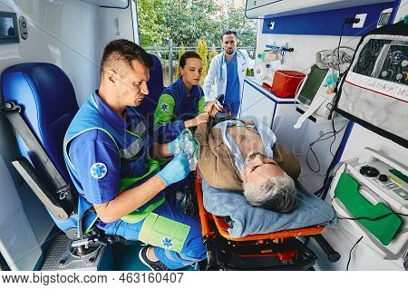 Paramedics Performing Electrocardiogram On Mature Patient Lying On Gurney With Electrodes Placed On 