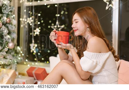 Young Smiling Beautiful Asian Woman Relax Smell Aromatic A Cup Of Coffee Or Tea In House With Christ